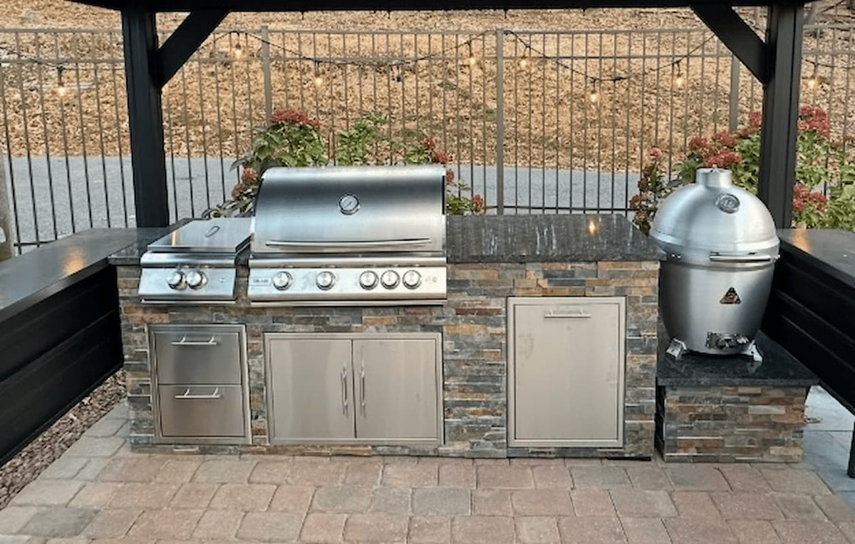 Outdoor kitchen with stainless steel grill and smoker on a stone countertop.
