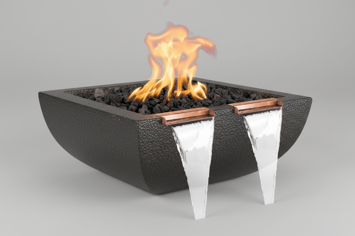 A modern square fire pit bowl with a textured black finish, filled with black stones and active orange flames, featuring two copper accents and dual clear waterfall spouts on a neutral gray background.