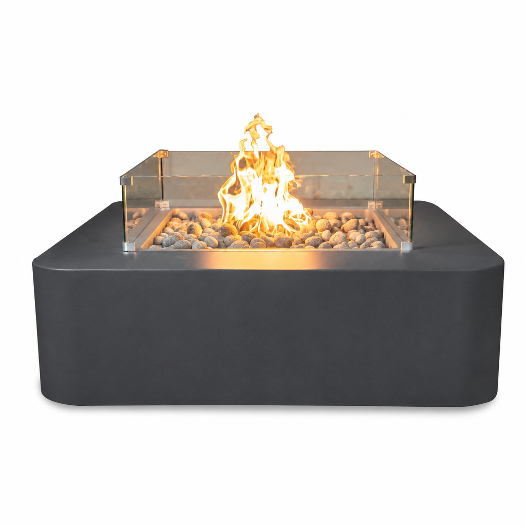 A modern square outdoor fire pit with a matte black base, clear glass wind guard, and active orange-yellow flame over decorative stones, shown on a plain white background.