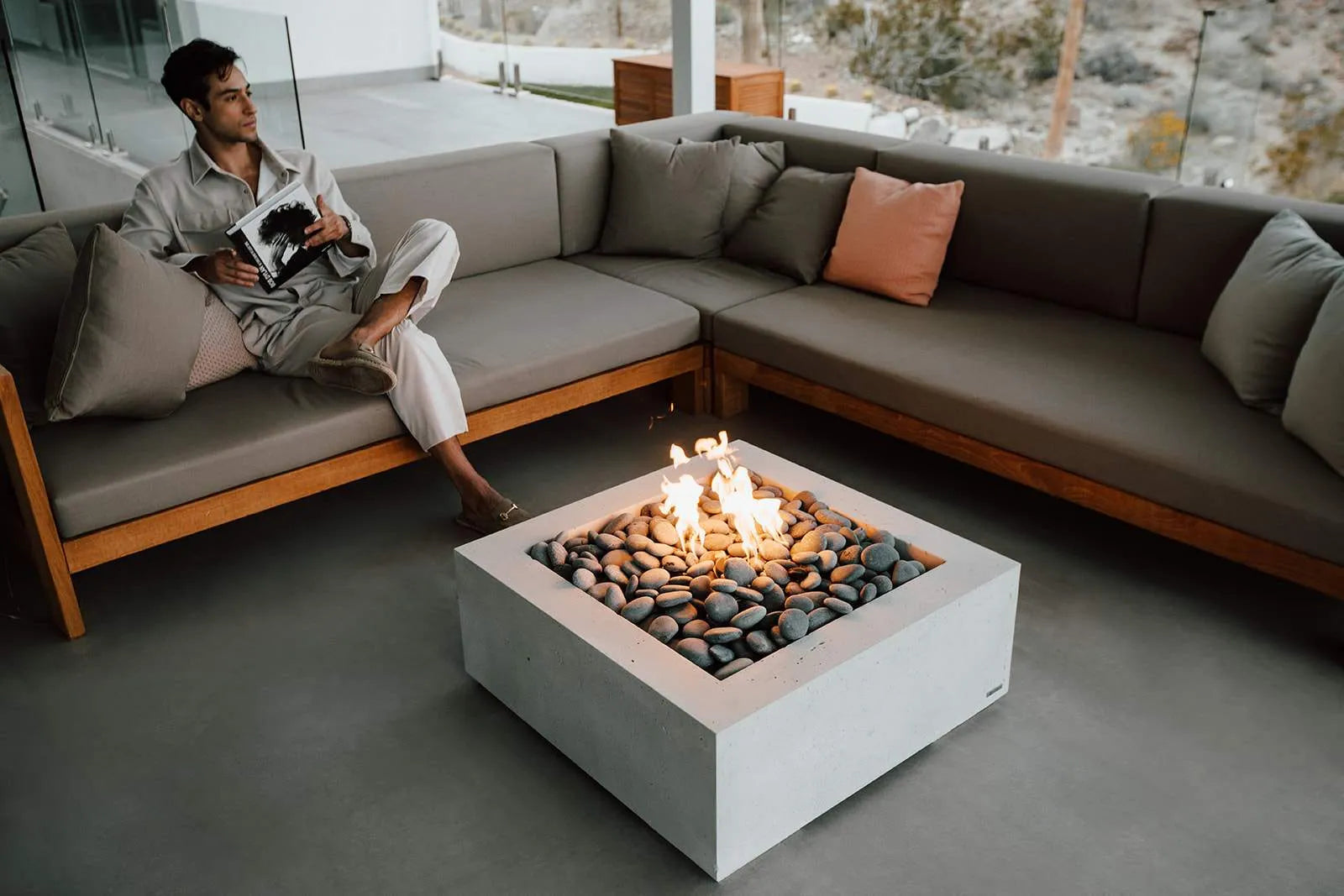 Man reading a book on a modern outdoor sofa with a fire pit table.