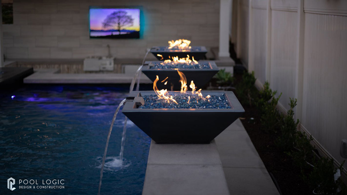 Outdoor fire pit by a pool with a television displaying a sunset scene.