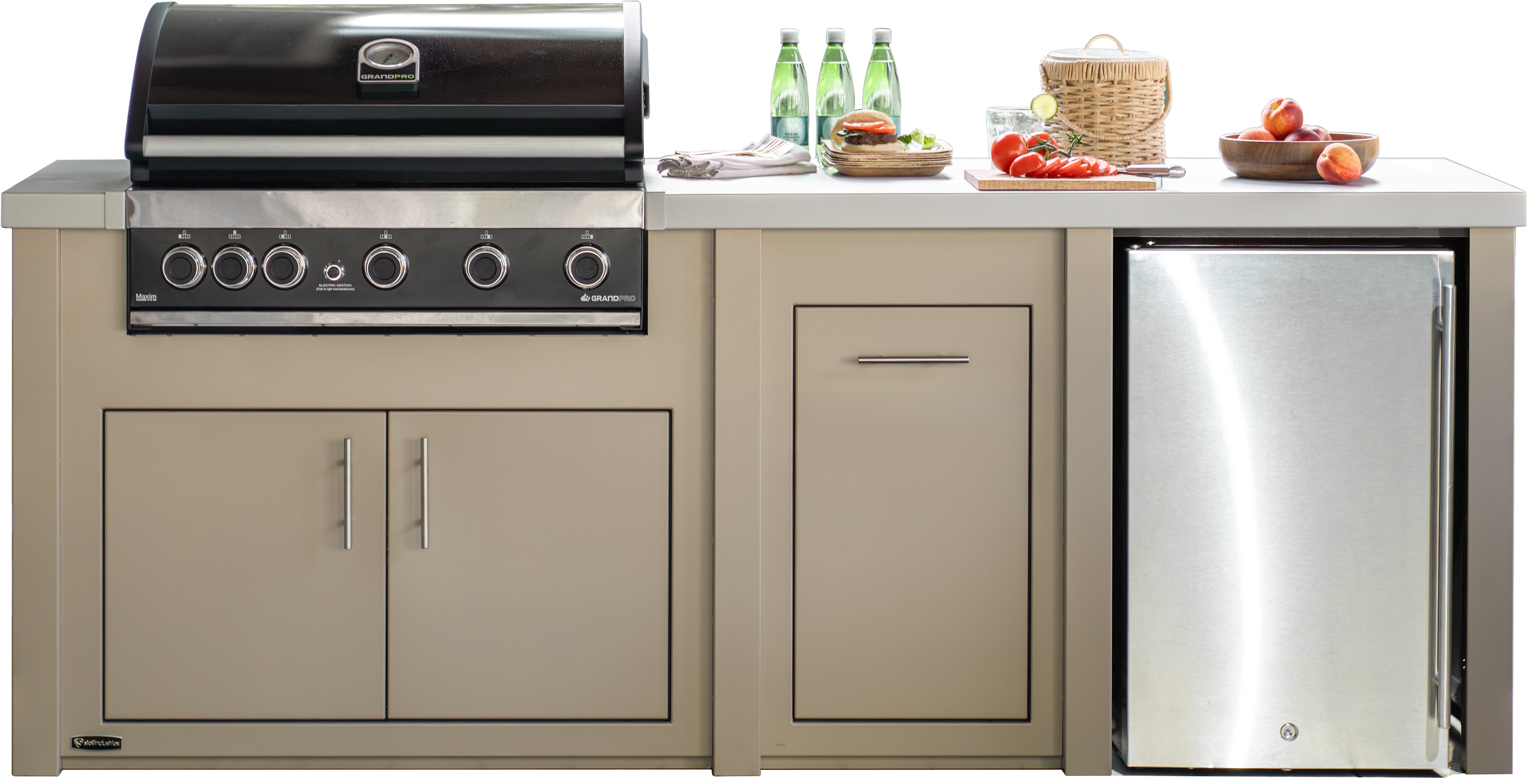 Outdoor kitchen island set featuring a built-in gas grill on the left, a stainless steel refrigerator on the right, and a central storage cabinet, all in a beige finish with a white countertop. Decorative food items and green bottles are placed on top.