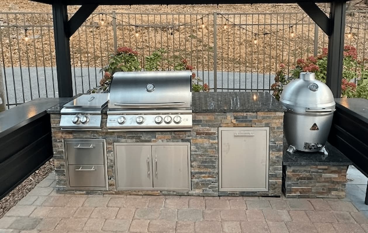 Outdoor kitchen with stainless steel grill and smoker on a stone countertop.