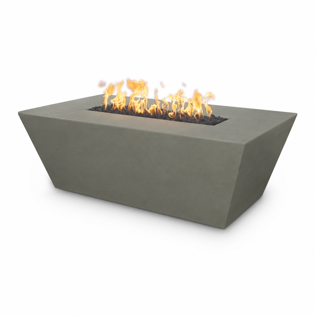 A modern rectangular concrete fire pit with a tapered triangular design, featuring orange flames burning over black fire glass inside, set against a plain white background.