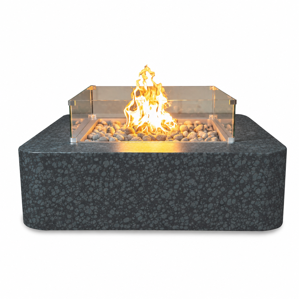A modern square outdoor fire pit with a dark speckled stone-look base, clear acrylic wind guard, and lit orange-yellow flame over decorative river rocks, shown on a plain white background.