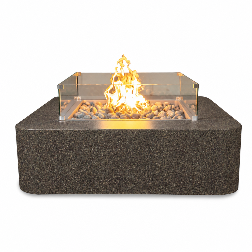 A rectangular outdoor fire pit with a dark textured stone-look base, clear acrylic wind guard, and glowing yellow-orange flame over decorative river rocks, shown on a plain white background.