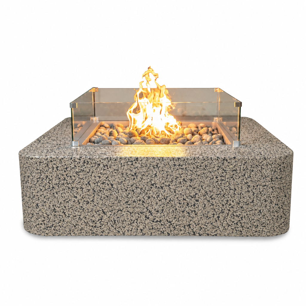 A rectangular outdoor fire pit with a speckled gray stone-look base, a clear glass wind guard, and a central flame effect over small stones, shown on a plain white background.