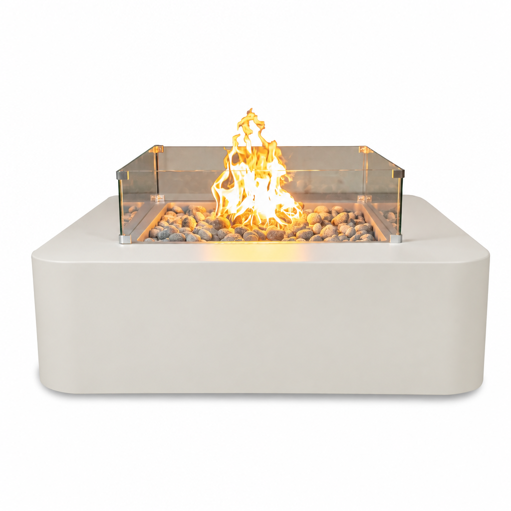 A modern rectangular outdoor fire pit table with a matte off-white base, a clear glass wind guard, and a glowing orange-yellow flame over decorative river rocks, shown on a solid white background.