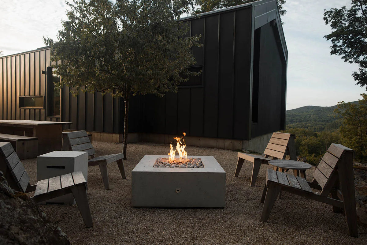 Outdoor setting with a fire pit, chairs, and a cabin in the background.