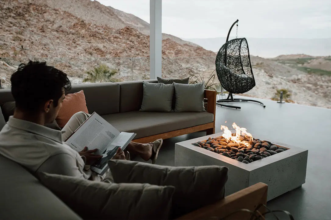 Person reading a book on a modern outdoor sofa with a fire pit in the background