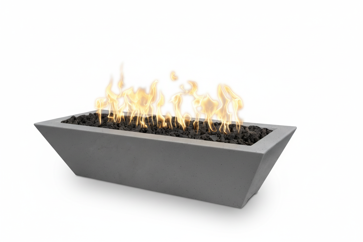 A modern rectangular concrete fire pit with a tapered triangular design, filled with black river rocks and lit with bright yellow and orange flames, shown on a solid white background.
