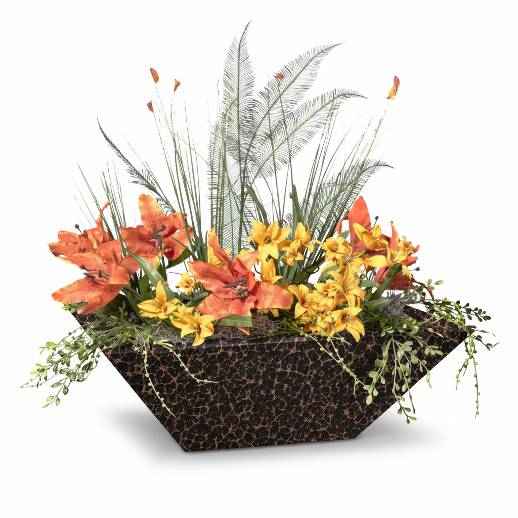 A geometric planter box filled with a mixed floral arrangement featuring orange and yellow lilies, green and silver foliage, and small trailing greenery, shown on a white background.