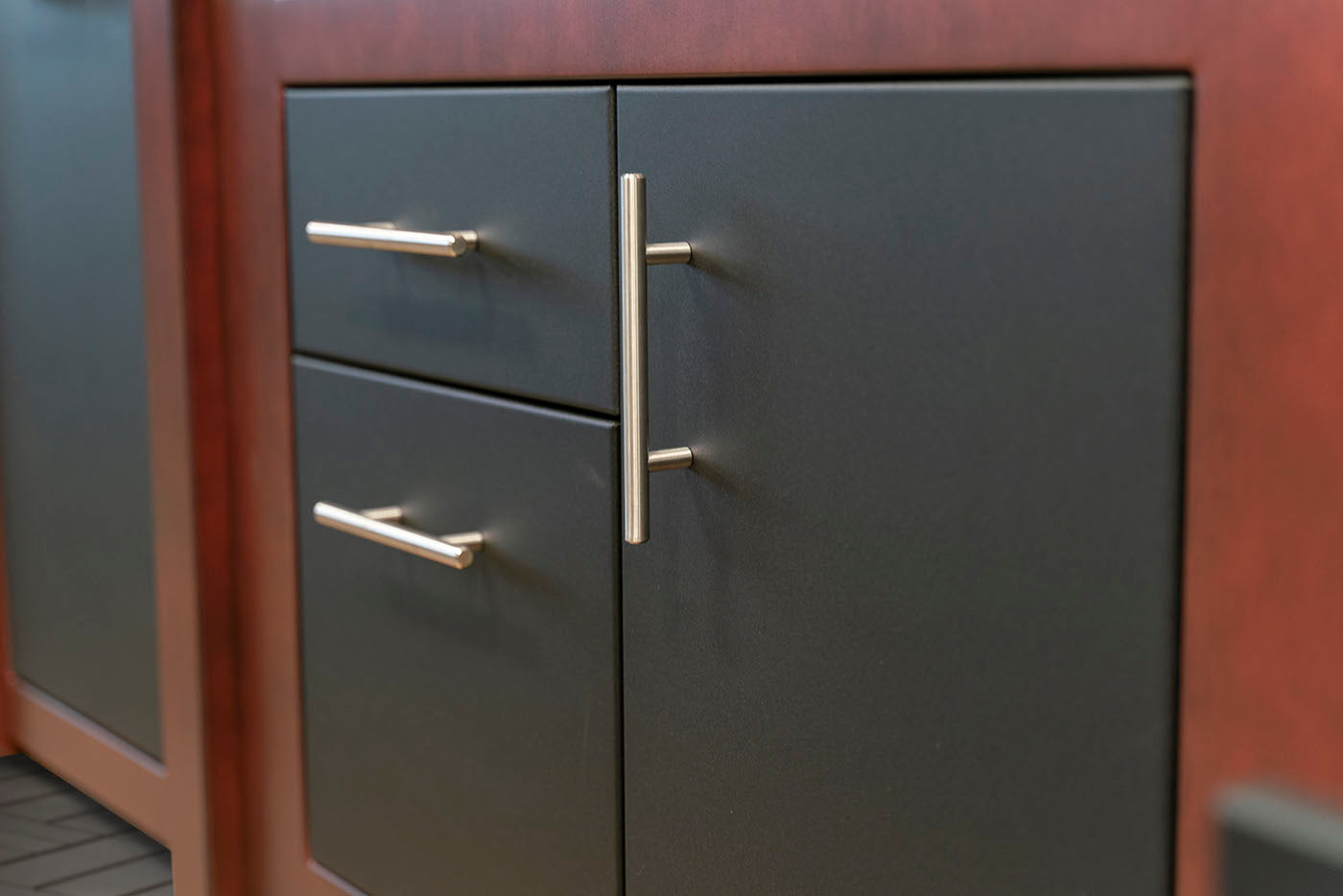 Dark charcoal gray cabinet doors with brushed gold metal handles, set within a reddish-brown wooden frame.
