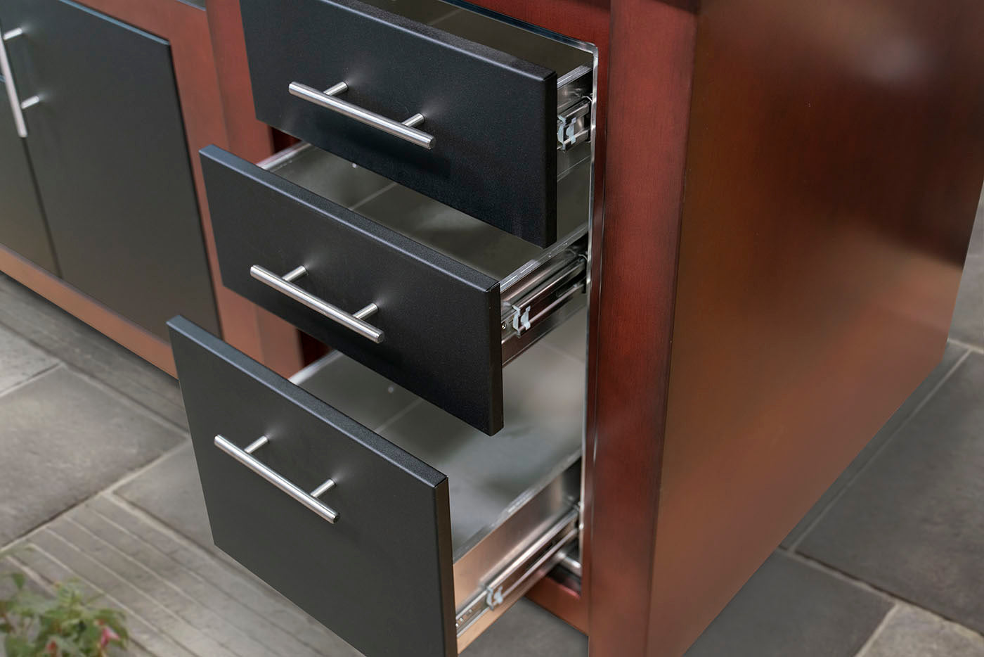 Close-up of a wooden cabinet with three black drawers pulled open, showing silver metal handles and interior drawer tracks.