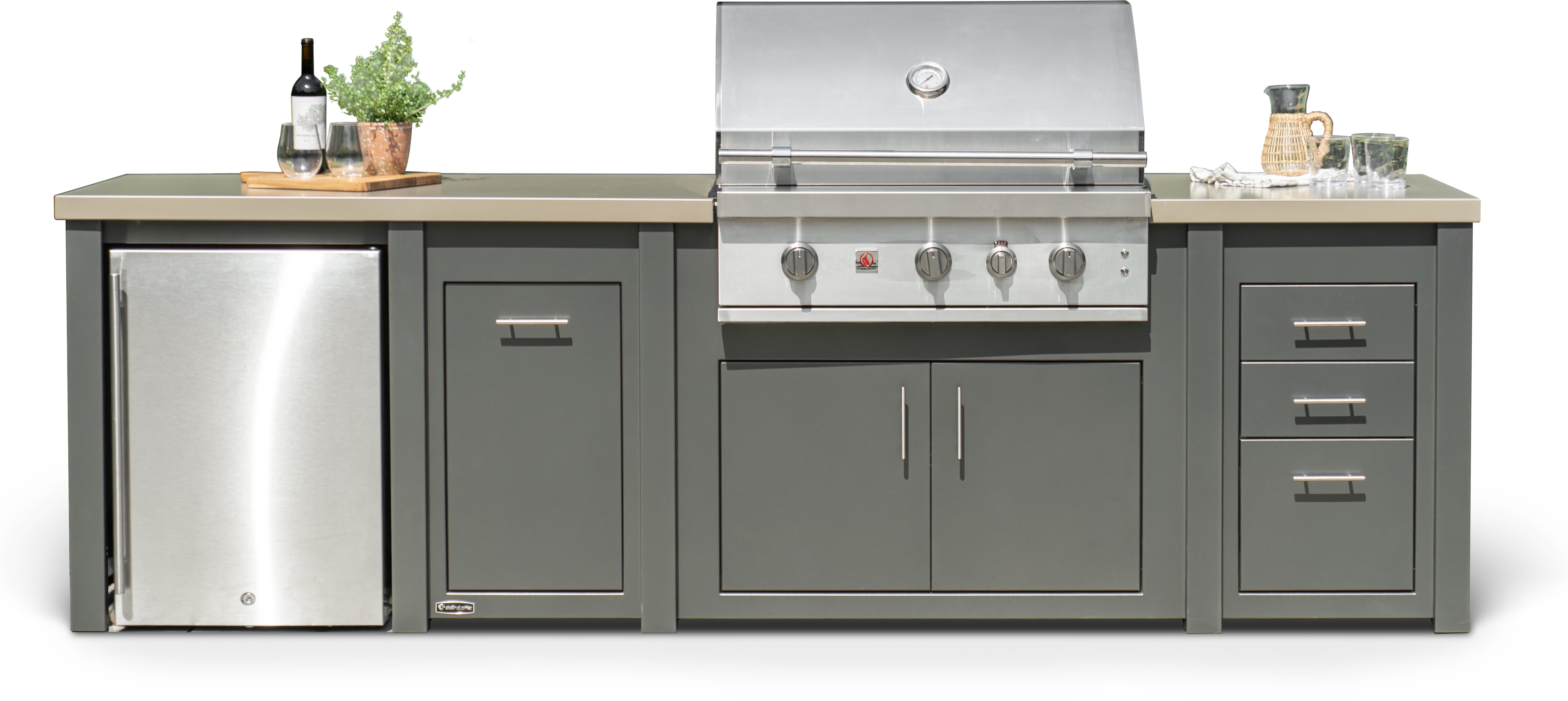 A stainless steel outdoor kitchen island set featuring a built-in gas grill, a mini-fridge, cabinets, drawers, and light beige countertops, shown against a plain white background with decorative items on top.