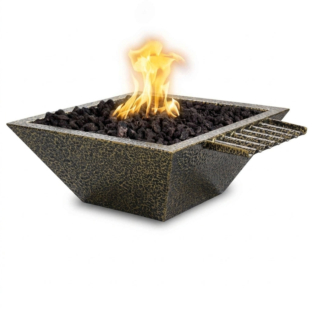 A square outdoor fire pit with a textured dark gray and black finish, filled with black lava rocks and showing a bright yellow and orange flame. A metal grate is attached on the right side, all set against a plain white background.